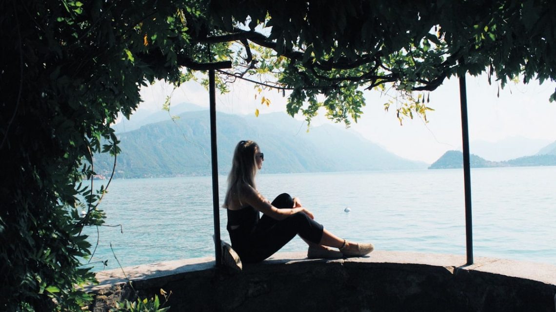 woman sitting on balustrade near body of water